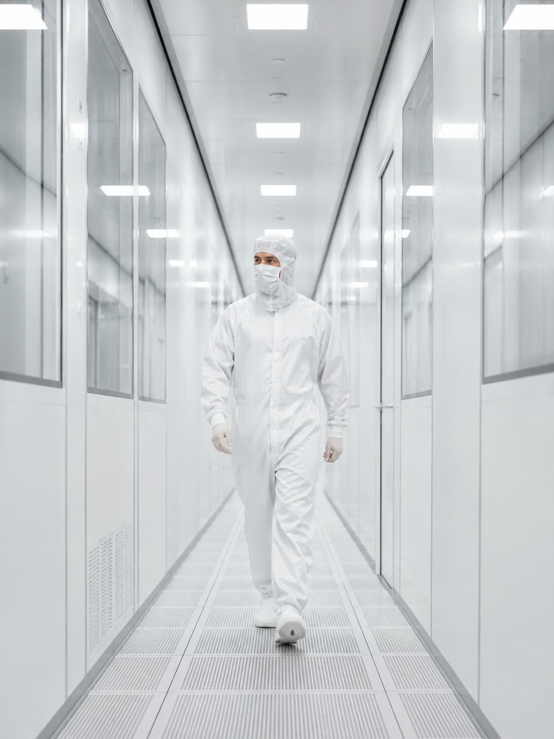 Technikerin im weissen Schutzanzug in einem hell beleuchteten Reinraumkorridor